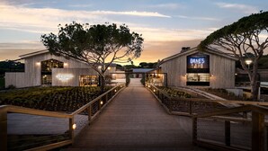 Un bâtiment moderne doté d’une terrasse en bois menant à une entrée sécurisée par un portail, le tout entouré d’arbres.
