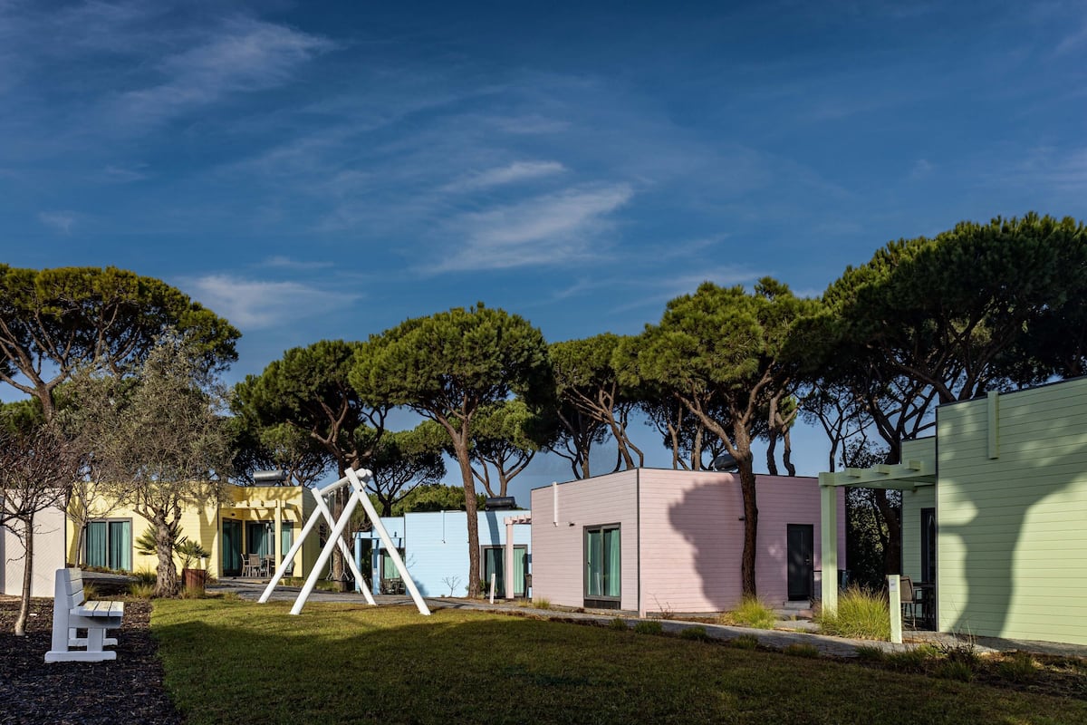 Una hilera de cabañas modernas de una sola planta, con un césped y árboles al fondo.