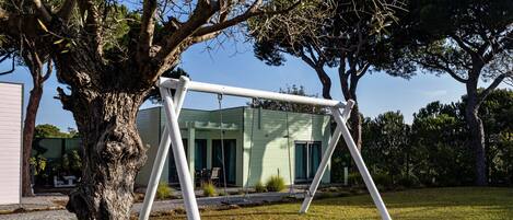 A swing set in a grassy yard with a house in the background.
