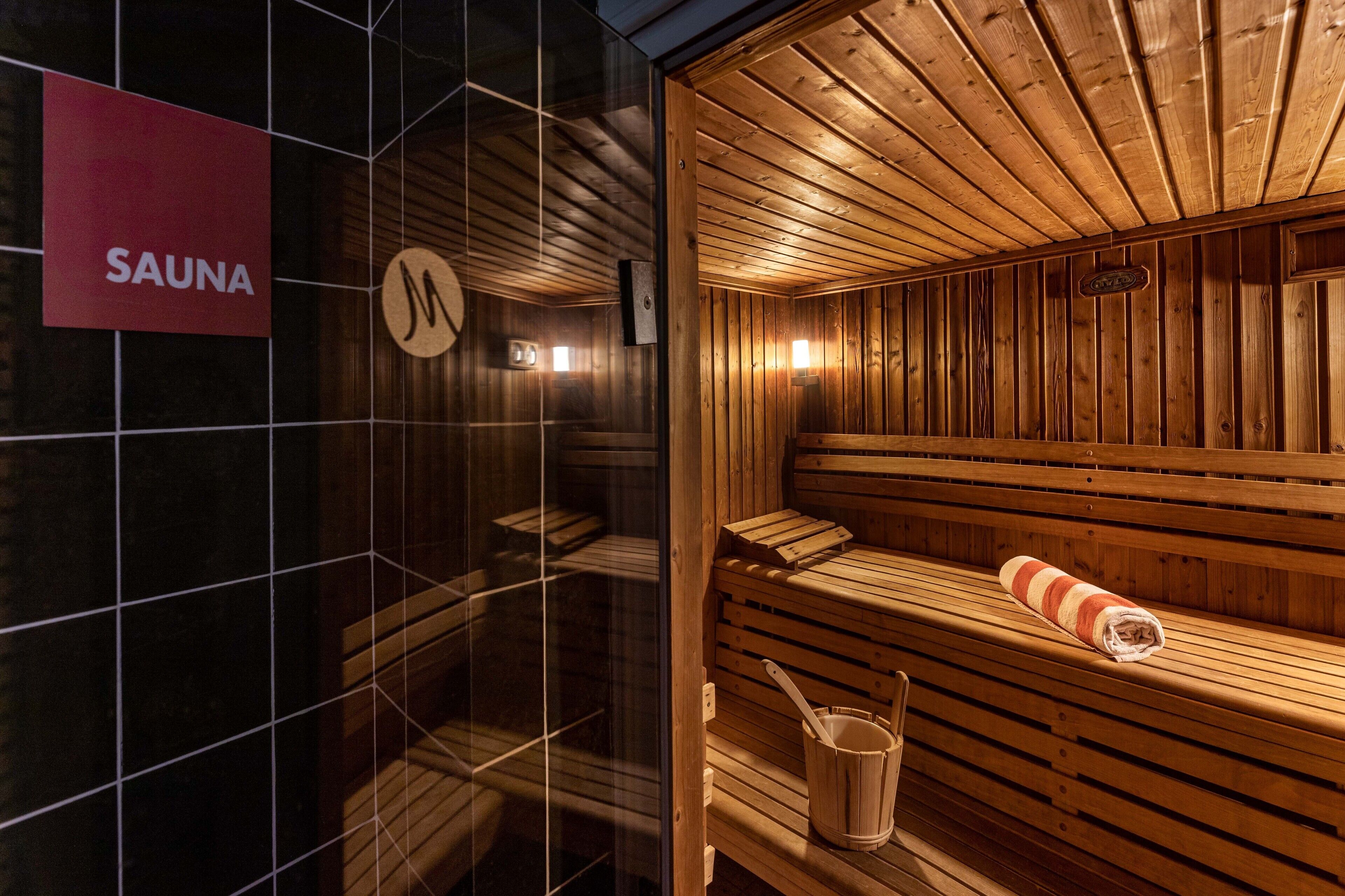 Una sauna con bancos de madera, un letrero que dice 'SAUNA' y un cubo de madera.