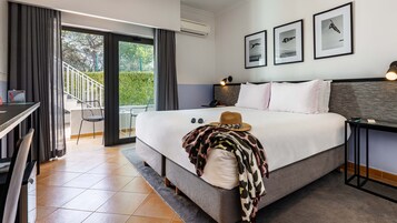 Habitación de hotel con cama, escritorio, silla y balcón con vistas a la vegetación.