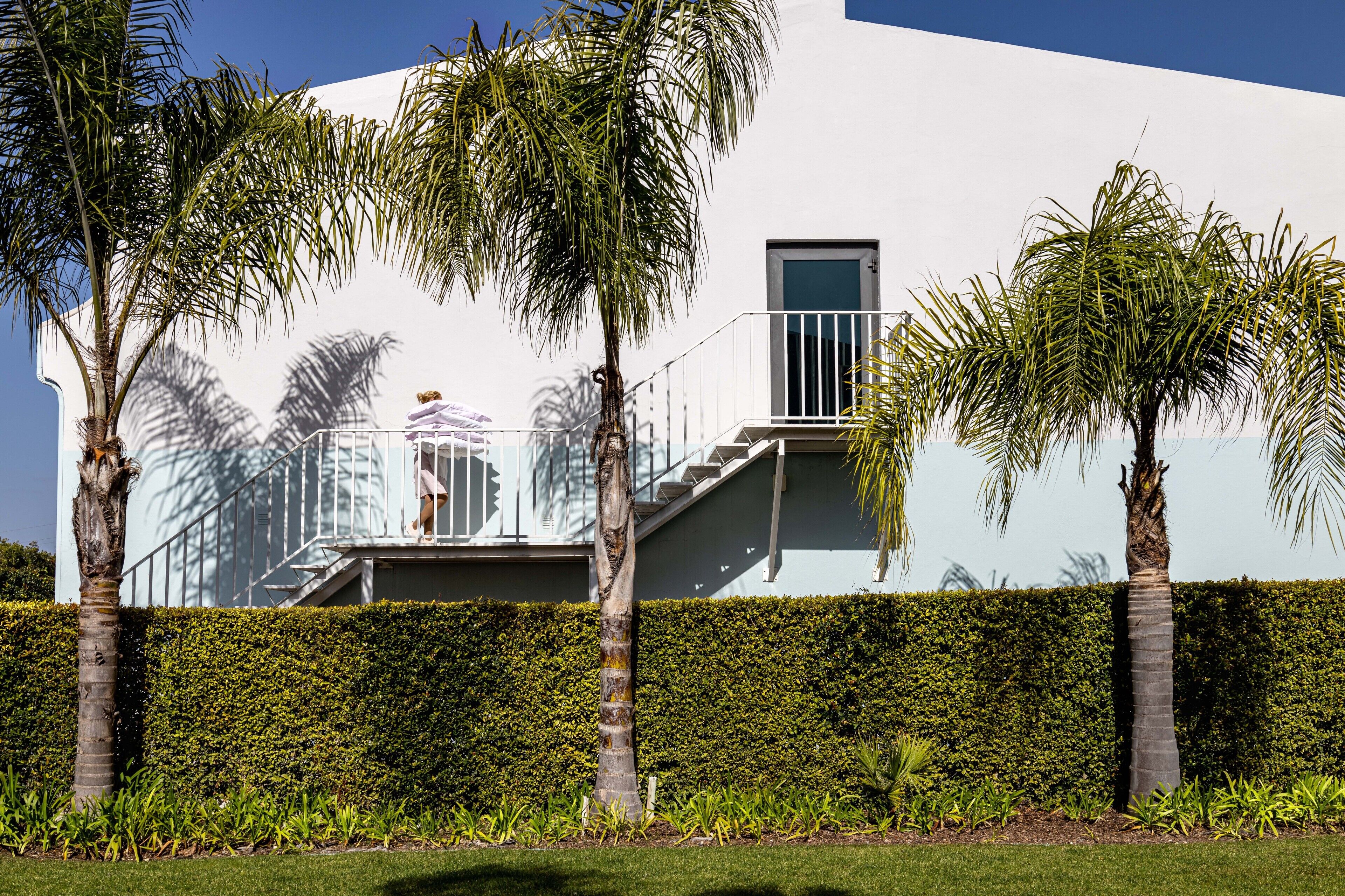 Um edifício moderno com fachada branca, varanda e palmeiras.
