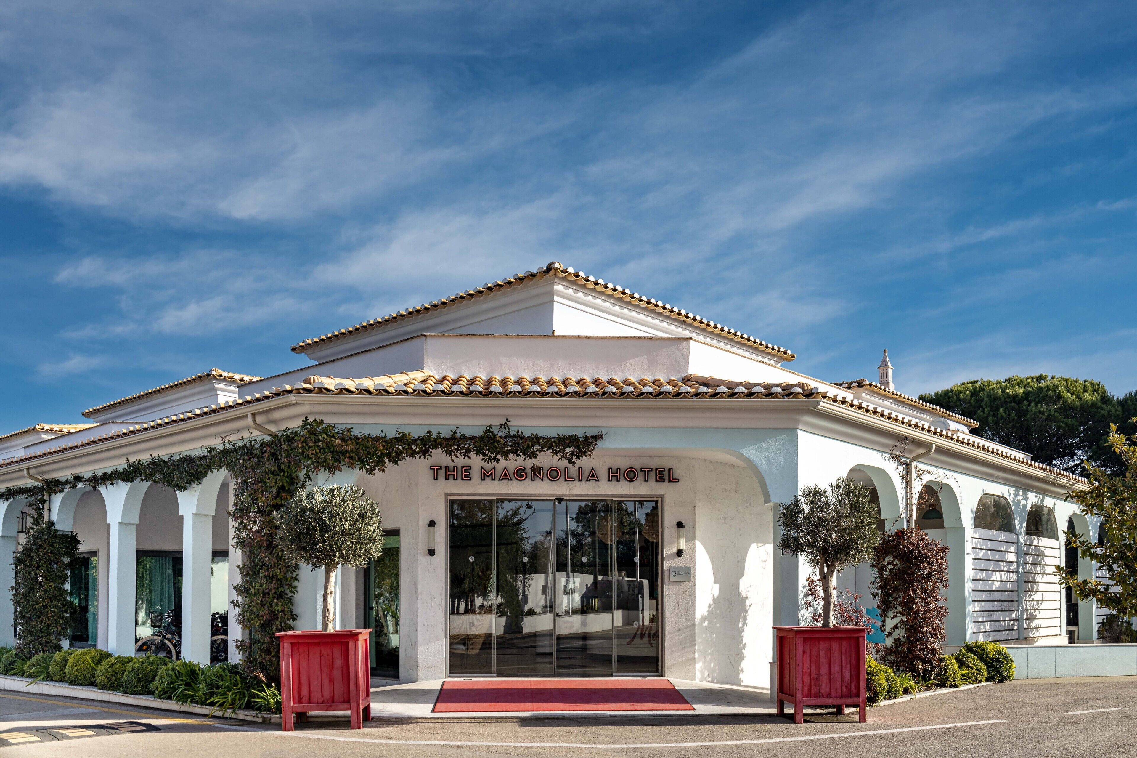 Das Magnolia Hotel mit heller Fassade, Rundbogenfenstern und rotem Teppich vor dem Eingang.