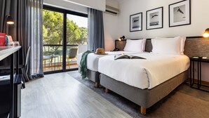 Une chambre d’hôtel moderne dotée d’un grand lit, d’un bureau avec une chaise, d’un coin repas avec des chaises et d’un balcon offrant une vue sur les arbres.