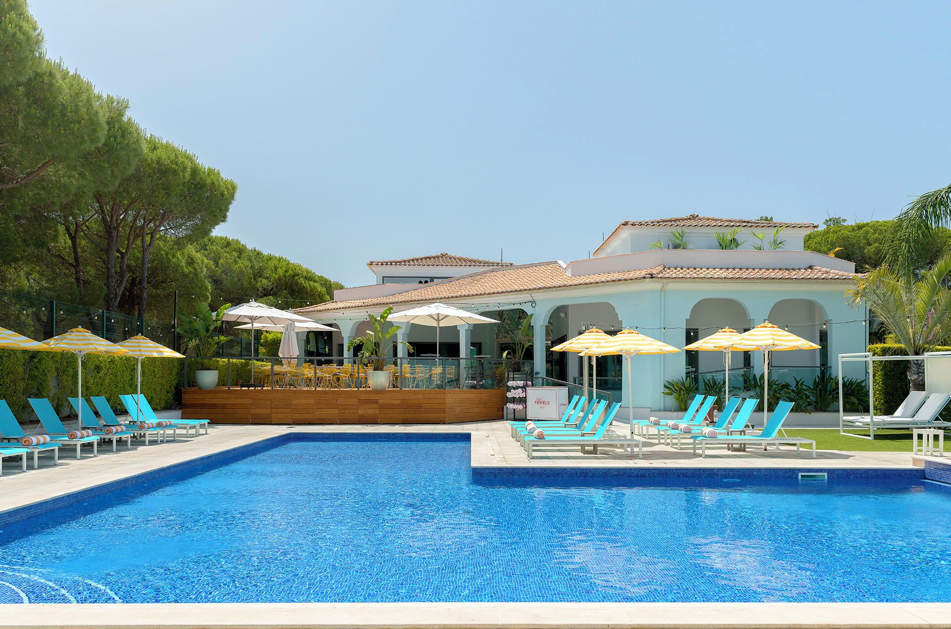 A swimming pool with lounge chairs and umbrellas, a building with arches, and greenery in the background.