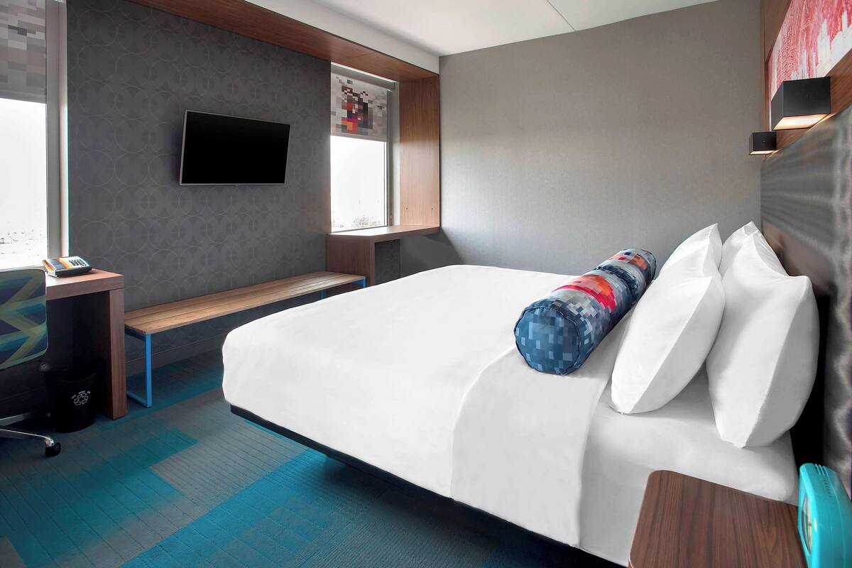 Une chambre d’hôtel avec un grand lit, un bureau avec un ordinateur, un téléviseur fixé au mur et une fenêtre donnant sur la ville.