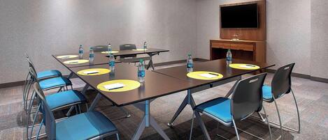 A conference room with a large table, chairs, water bottles, and a TV on the wall.