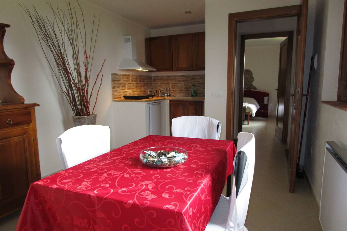 A dining area with a red tablecloth, white chairs, a decorative bowl, and a brick backsplash.