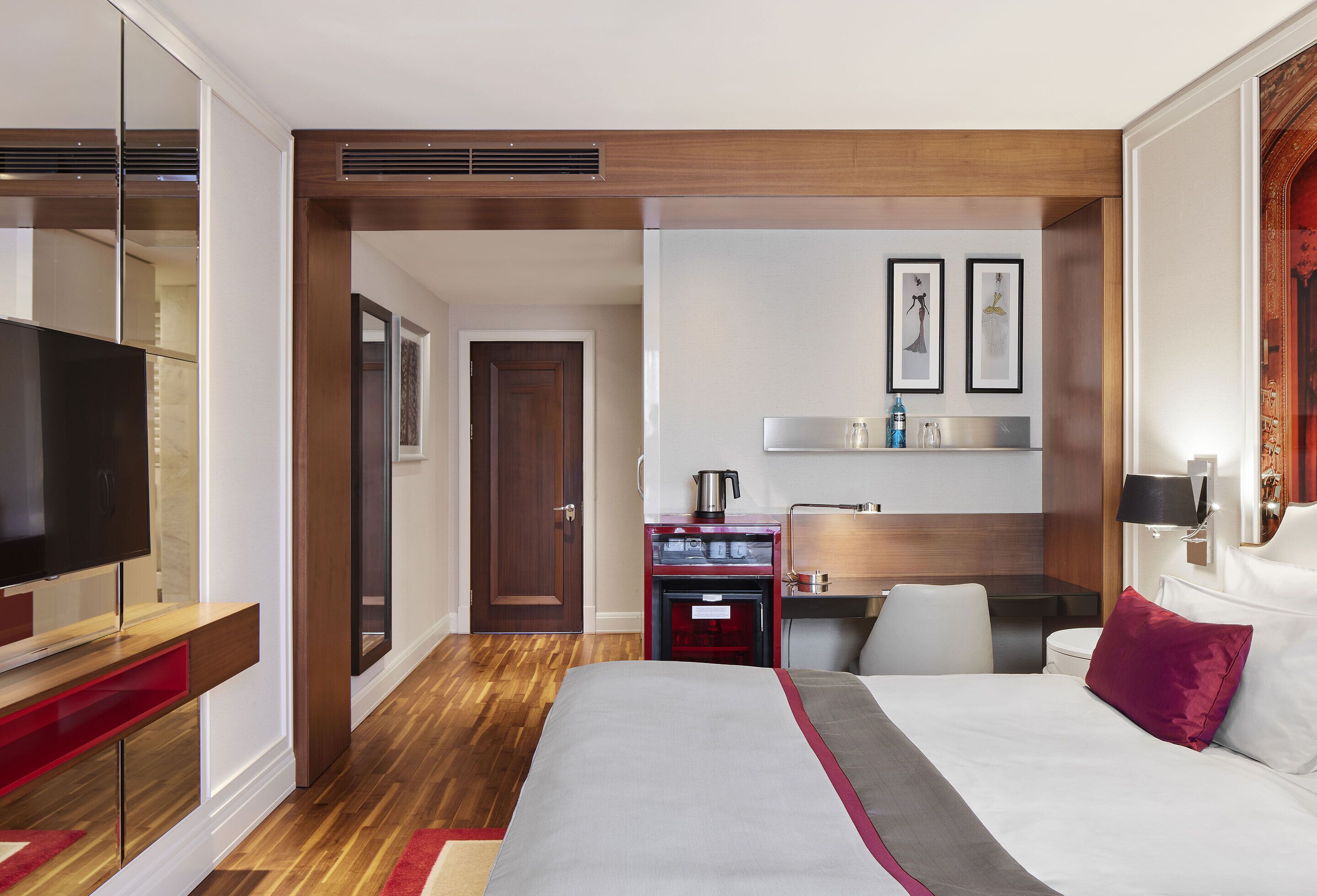 Habitación de hotel con cama, televisión, escritorio con silla, kitchenette pequeño y baño.