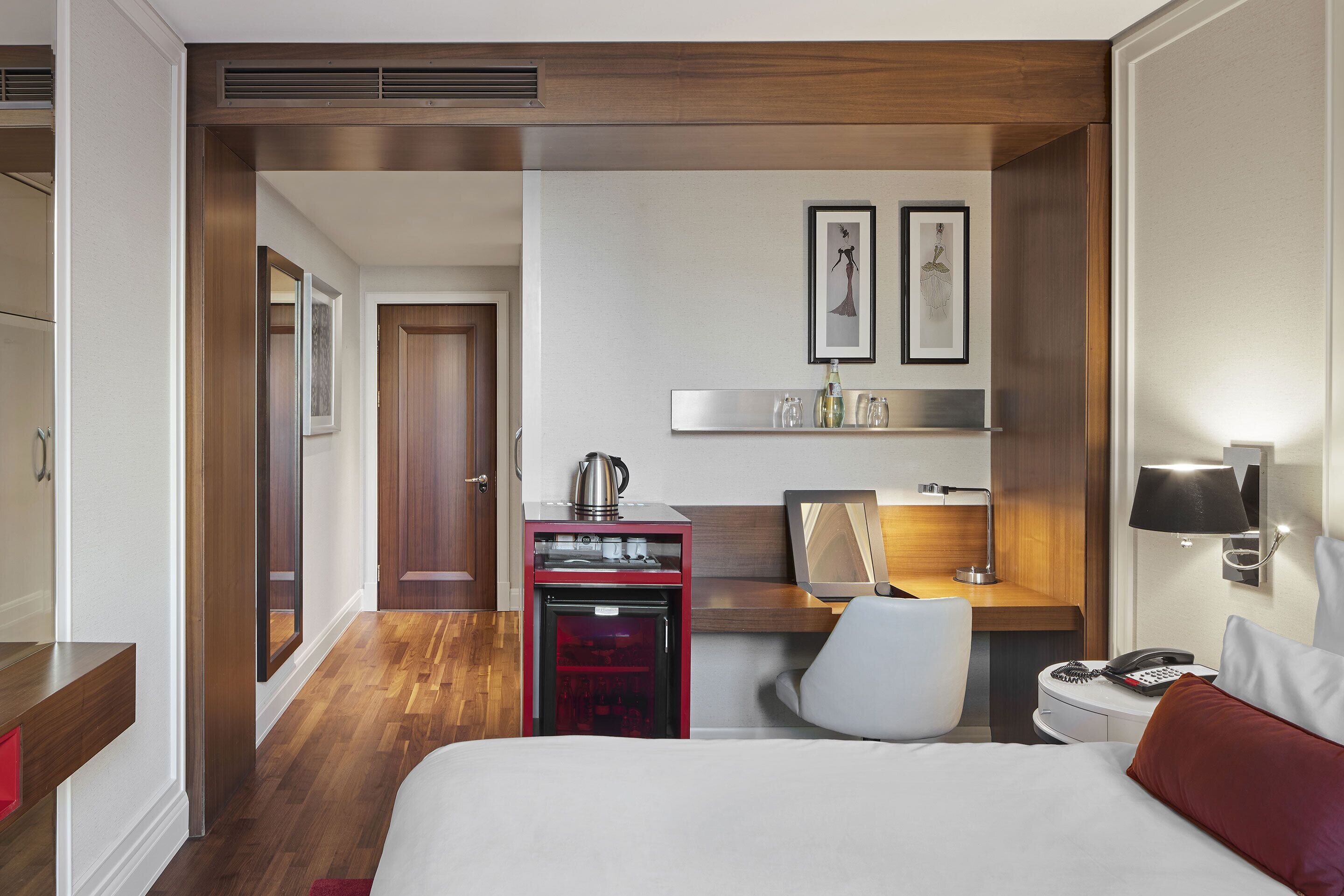 Una habitación de hotel con cama, escritorio, silla, kitchenette pequeña y espejo.