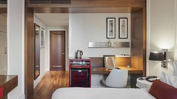 Una habitación de hotel con cama, escritorio, silla, kitchenette pequeña y espejo.