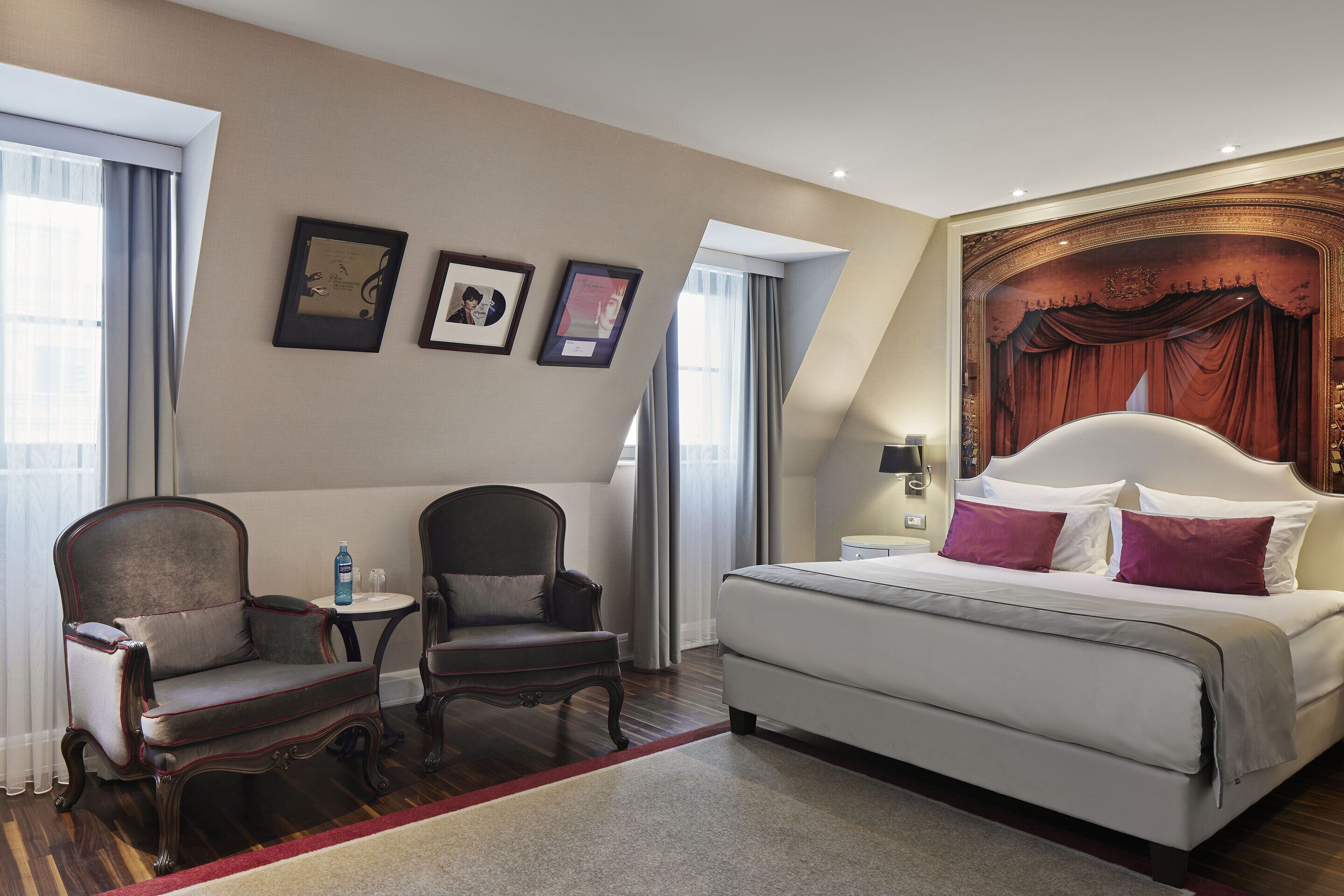 A hotel room with a large bed, two armchairs, a small table, and a window with curtains.