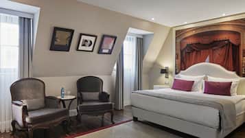 A hotel room with a large bed, two armchairs, a small table, and a window with curtains.