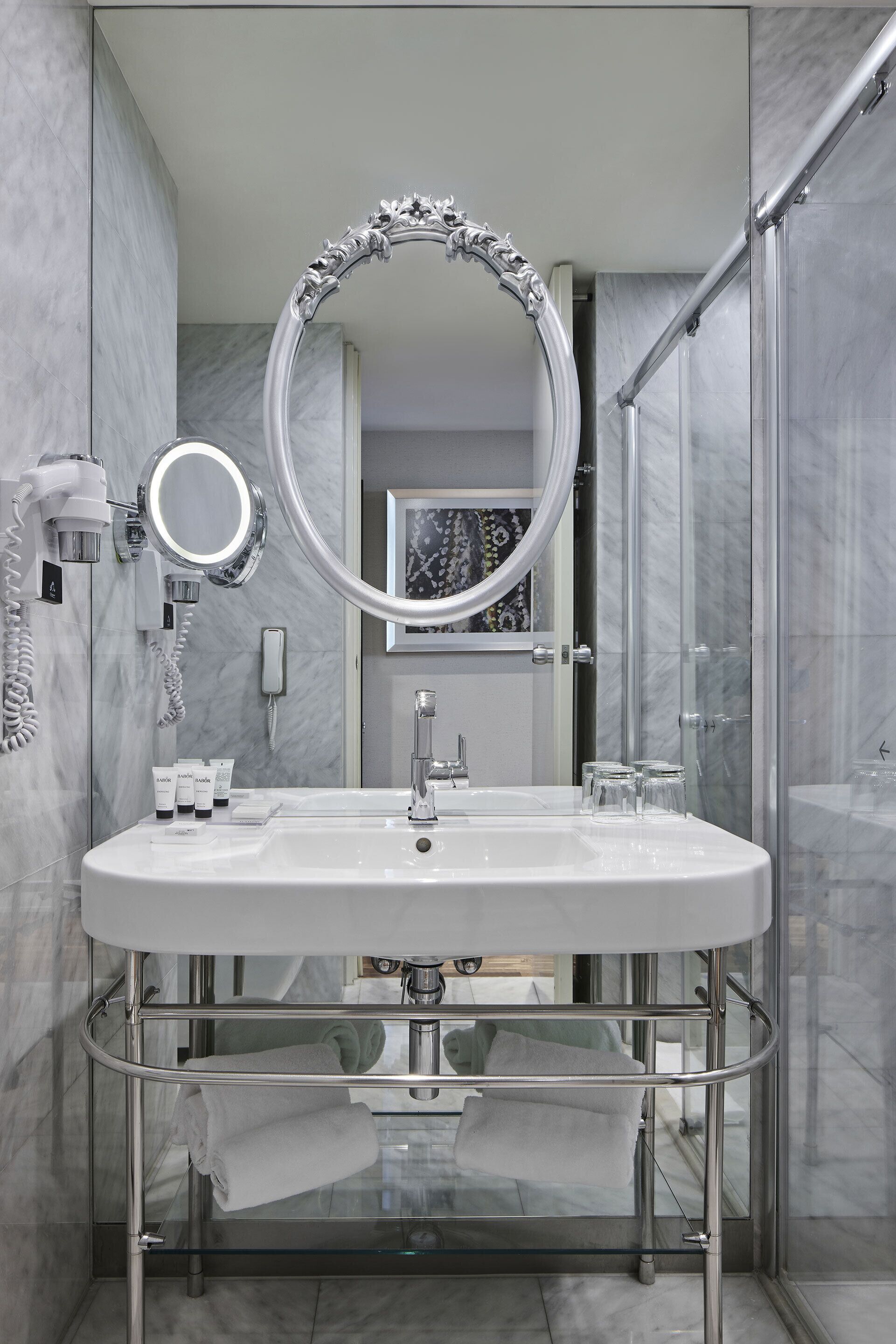 Un baño moderno con un espejo grande, cabina de ducha de vidrio y pared con azulejos de mármol.