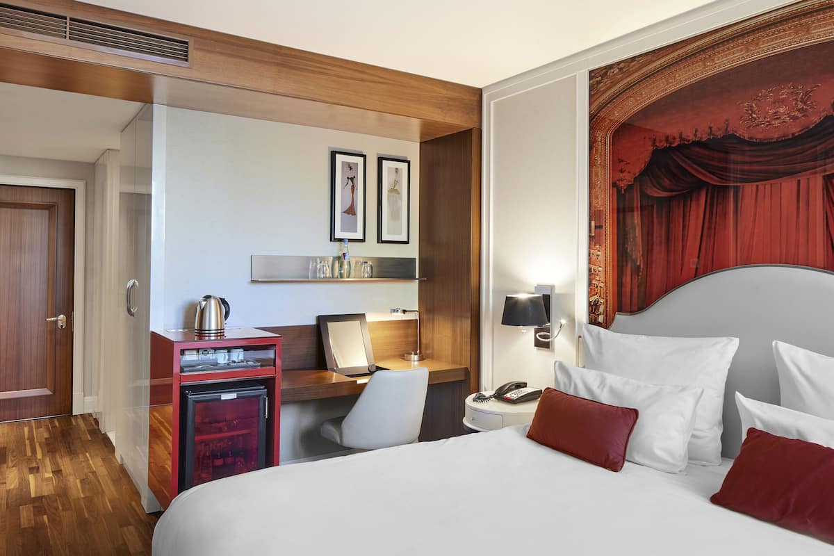 A hotel room with a bed, desk, chair, and a minibar.