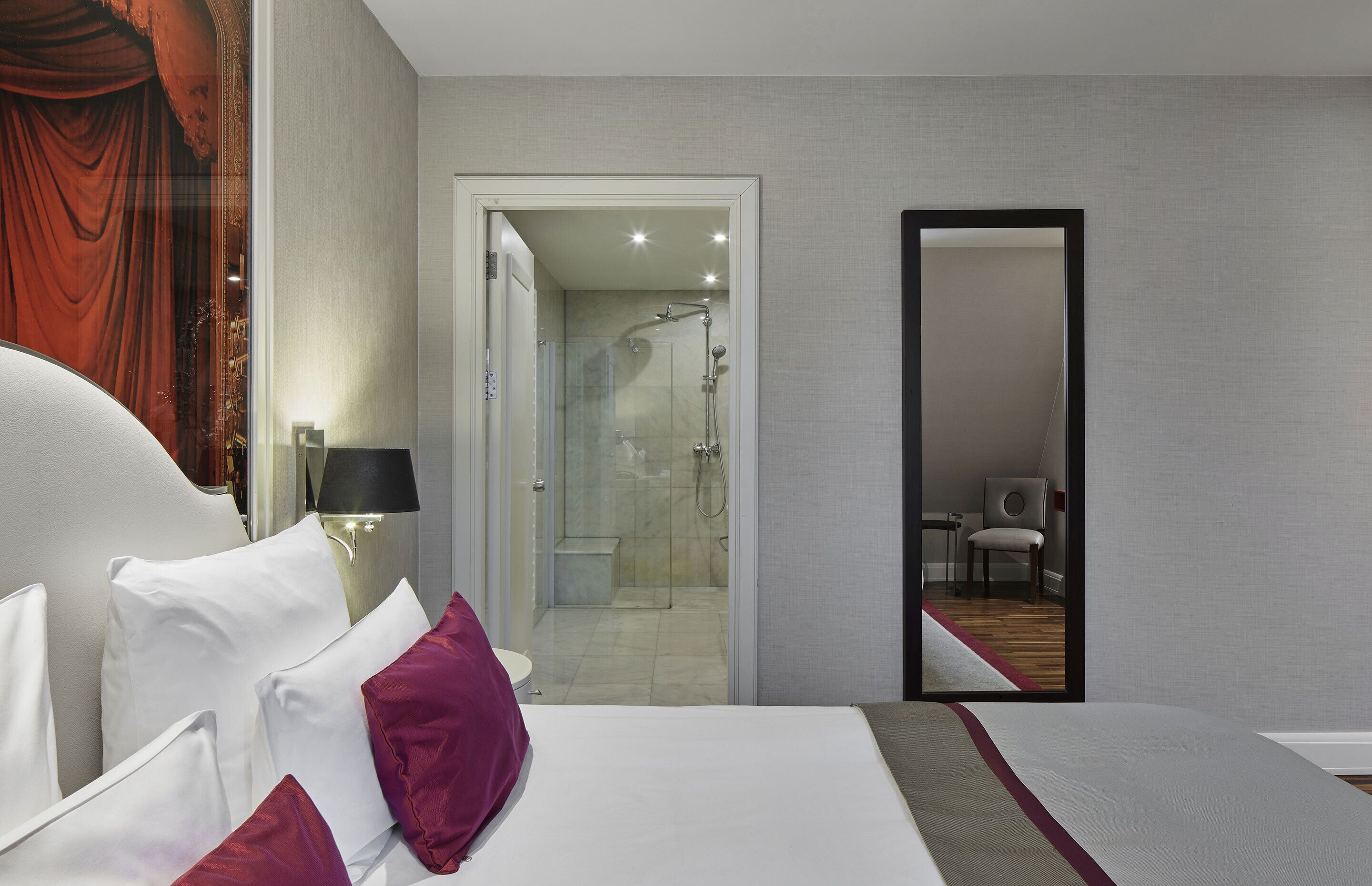 A hotel room with a bed, a nightstand with a lamp, a shower area, and a mirror.