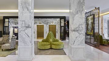 Un vestíbulo con columnas de mármol, una zona de estar tapizada en verde y una obra de arte enmarcada en la pared.