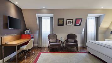 Una habitación de hotel con escritorio, dos sillones, cama y televisor.
