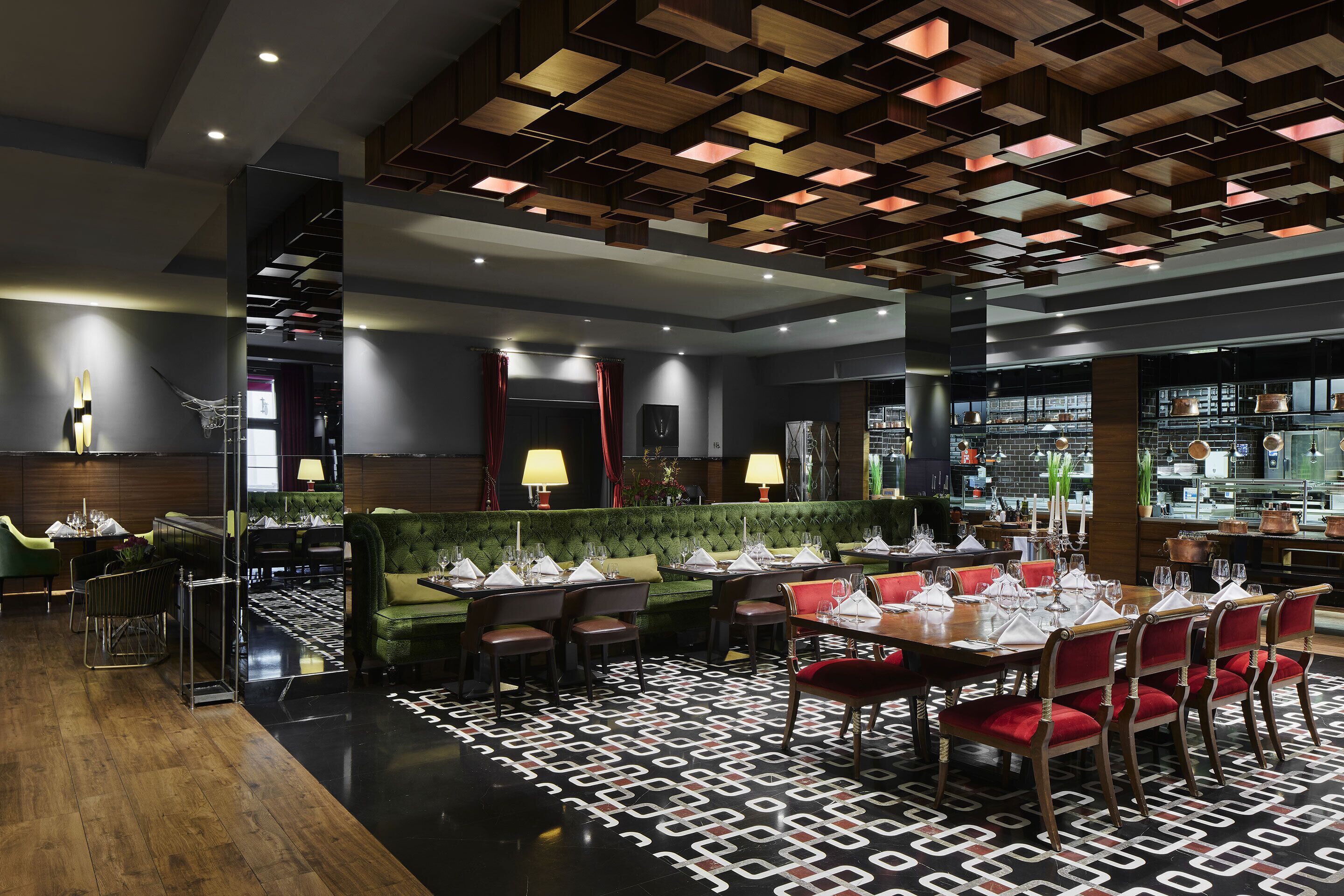 Un restaurante moderno con suelo de patrón geométrico, asientos tapizados en verde y diversas mesas dispuestas para recibir a los comensales.