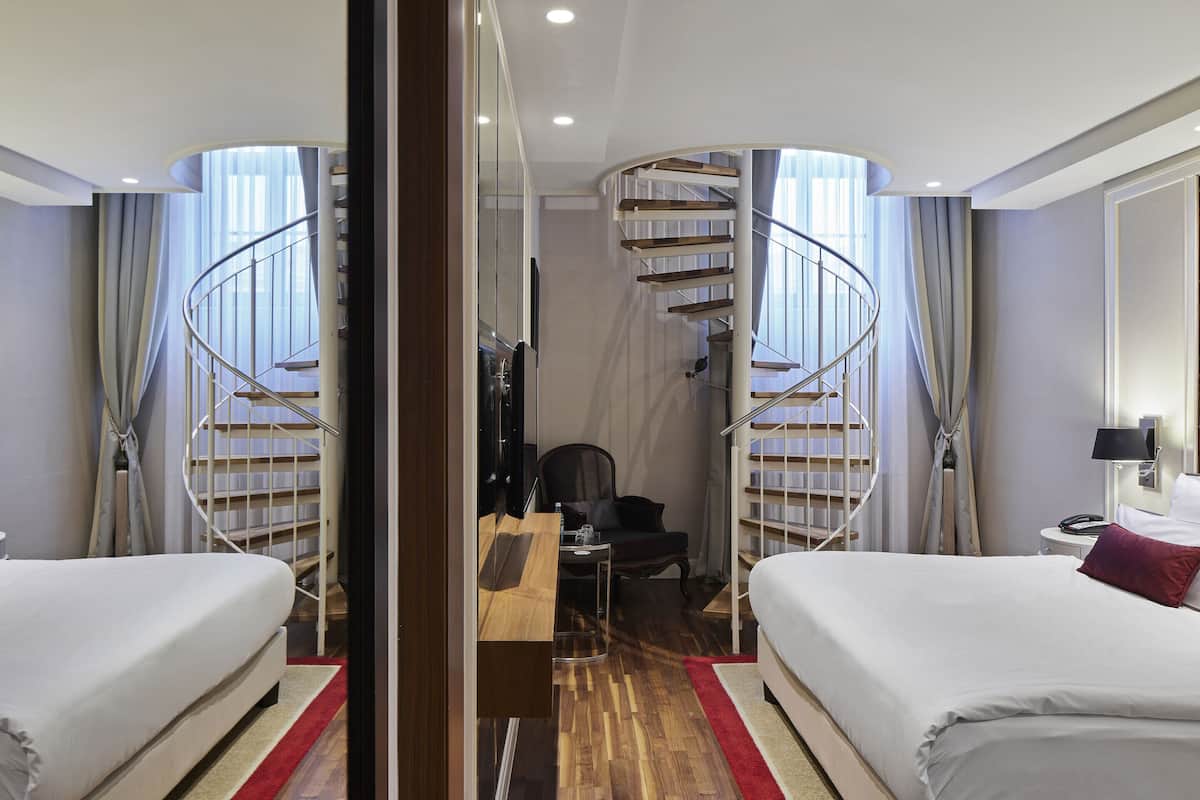 A hotel room with a spiral staircase, two beds, a desk, and a chair.