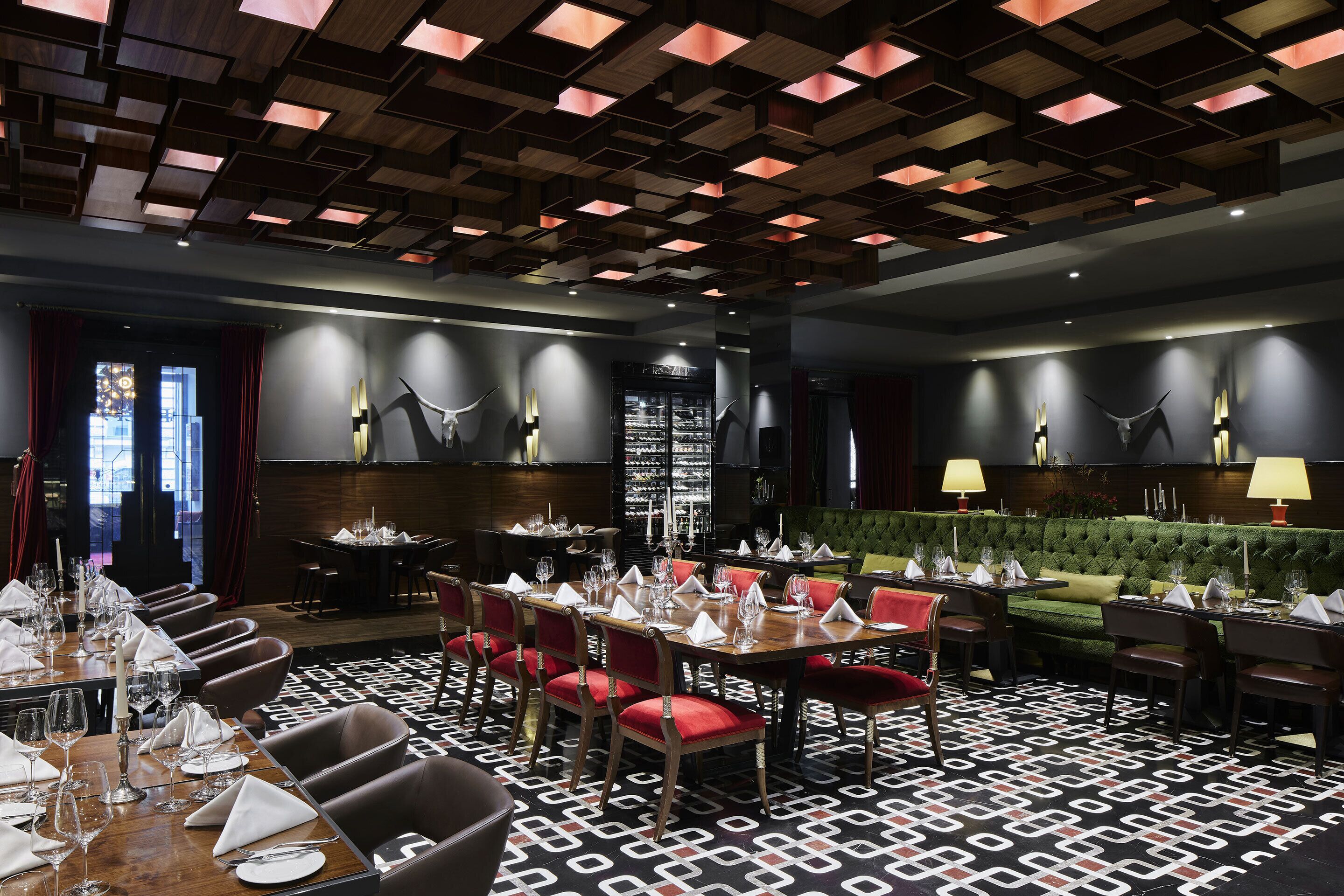A dining area with tables set for service, red upholstered chairs, and a patterned floor.