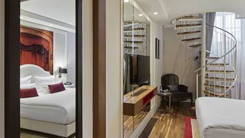 A hotel room with a bed, a desk, a chair, a TV, and a spiral staircase.