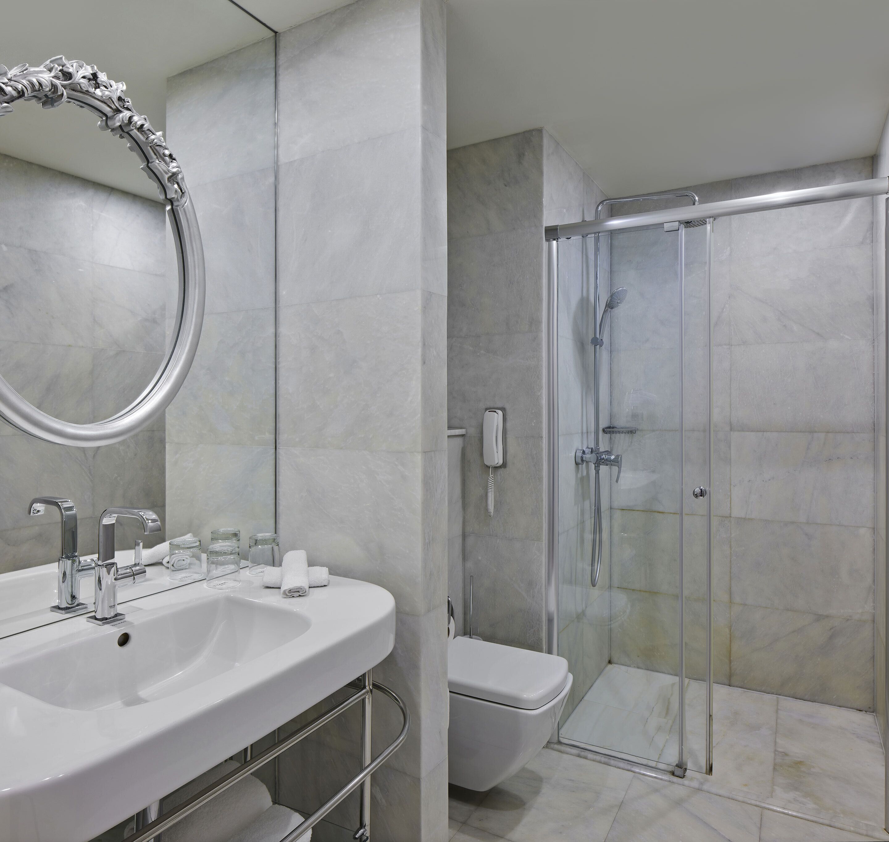 A modern bathroom with a white sink, two faucets, a mirror, and a glass-enclosed shower.