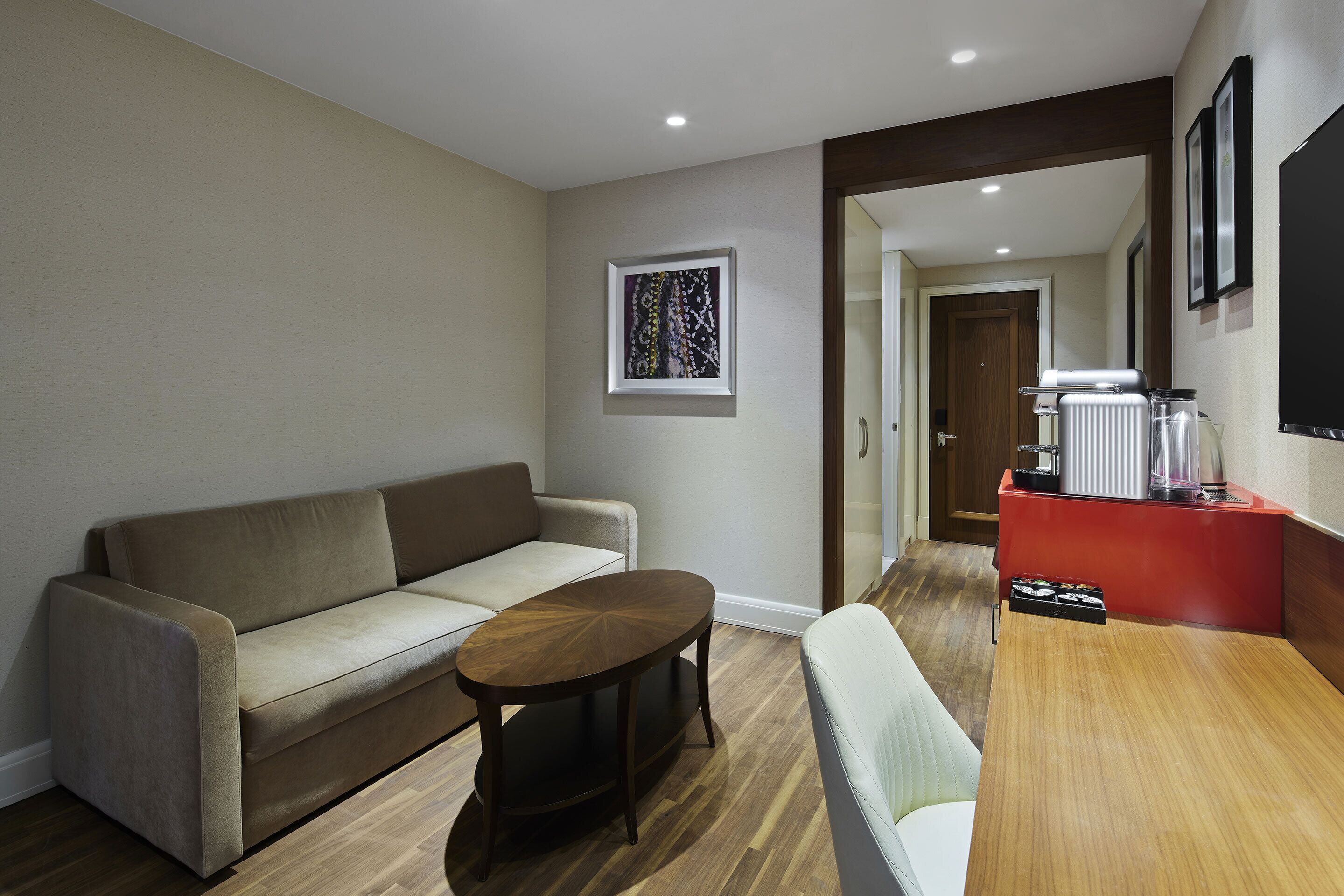Una sala moderna con un sofá, una mesa de centro y una mesa de comedor. Hay una zona de cocina con un refrigerador y un microondas.