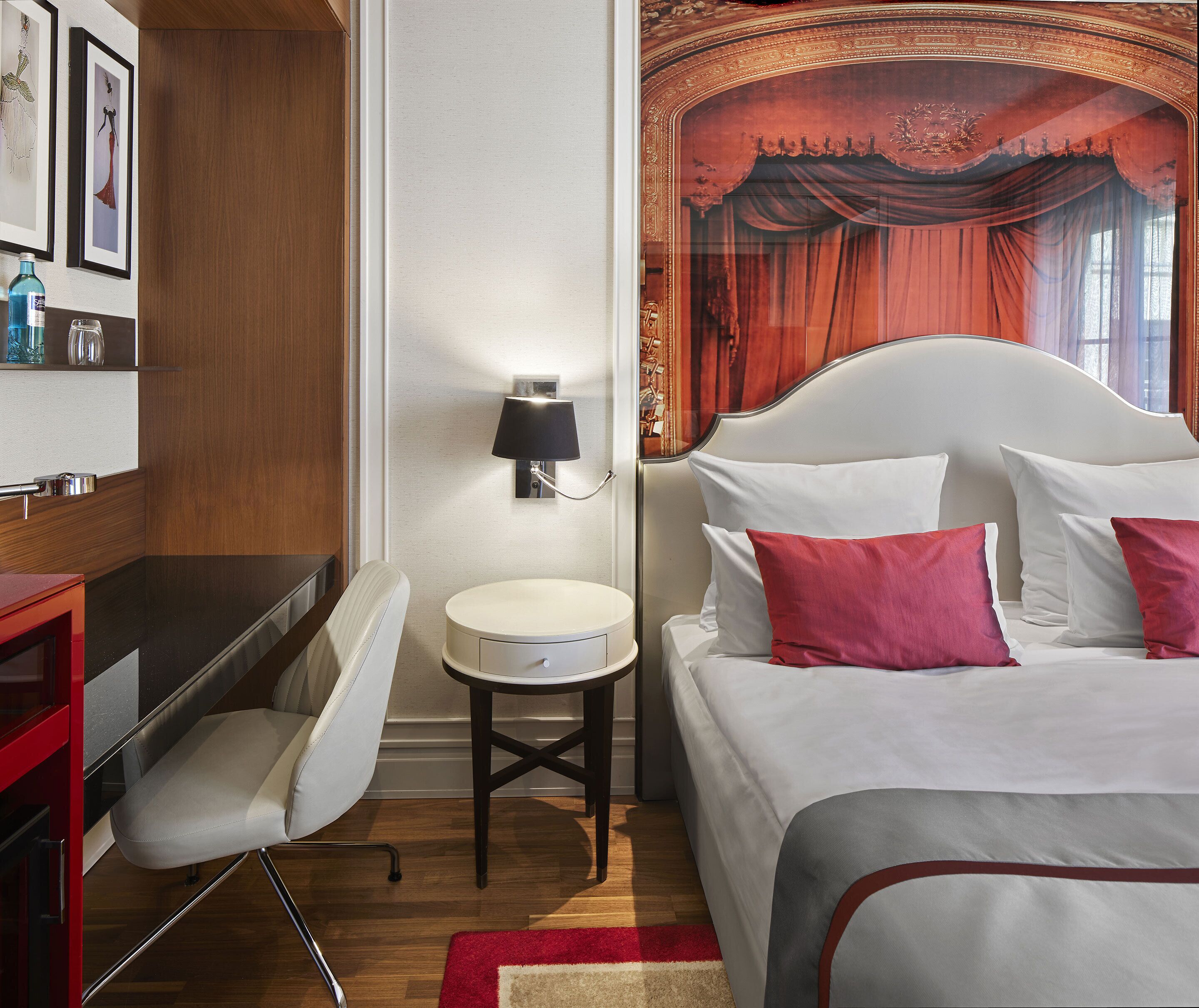 Habitación de hotel con cama, escritorio, silla, una mesita redonda y una lámpara de pared.