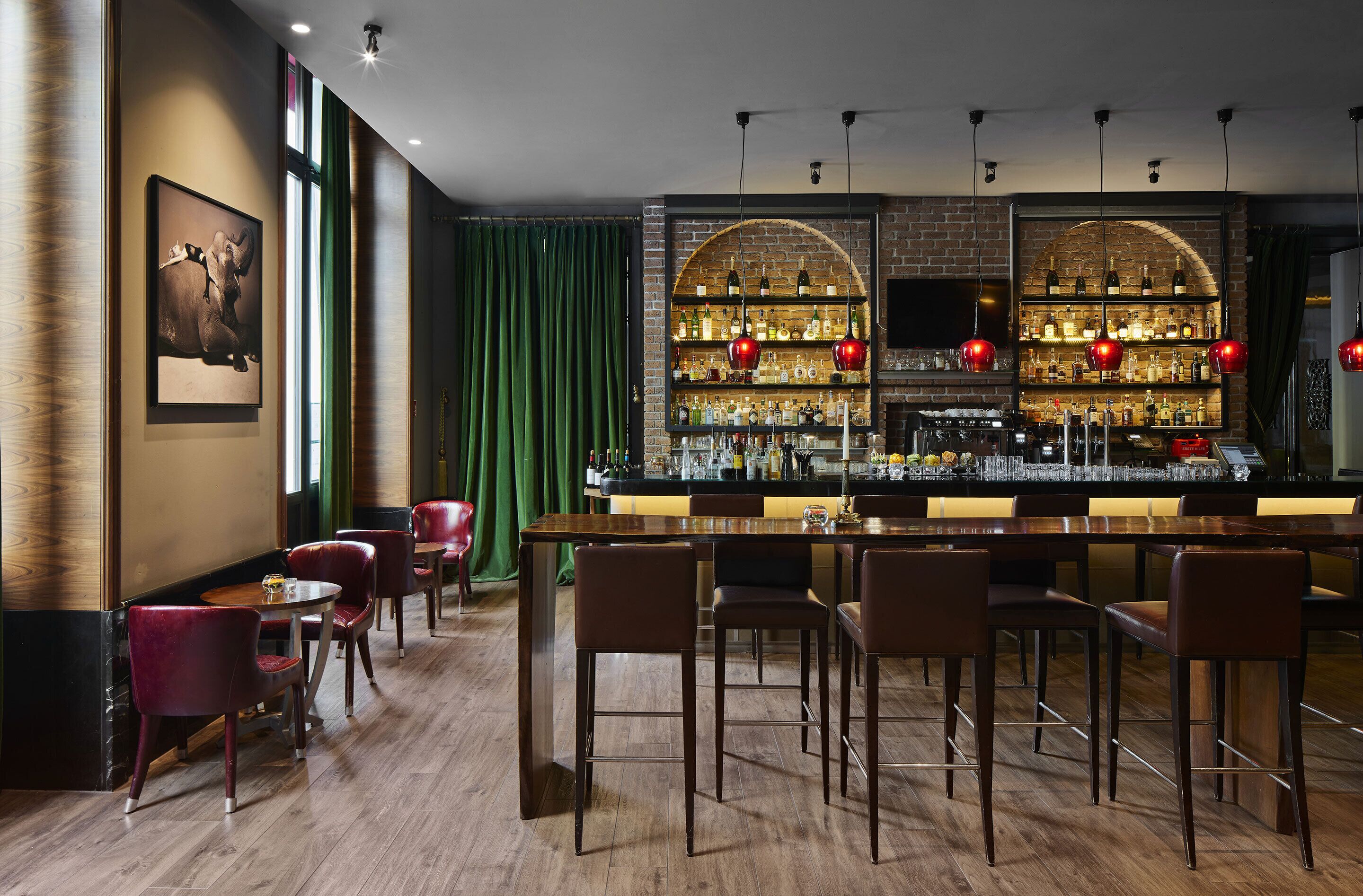 A bar area with wooden flooring, red chairs, and a bar counter with shelves of bottles.
