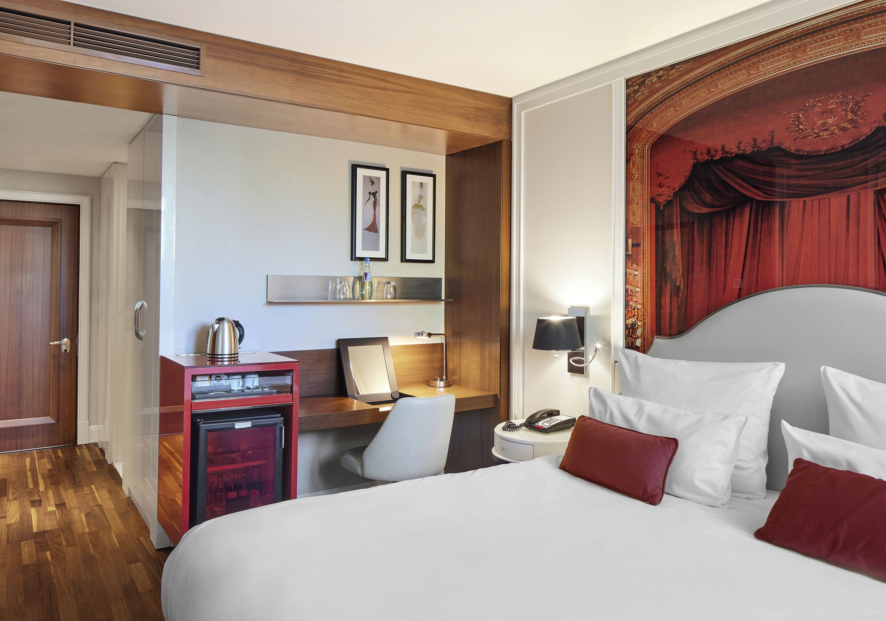 A hotel room with a bed, desk, chair, and a minibar.