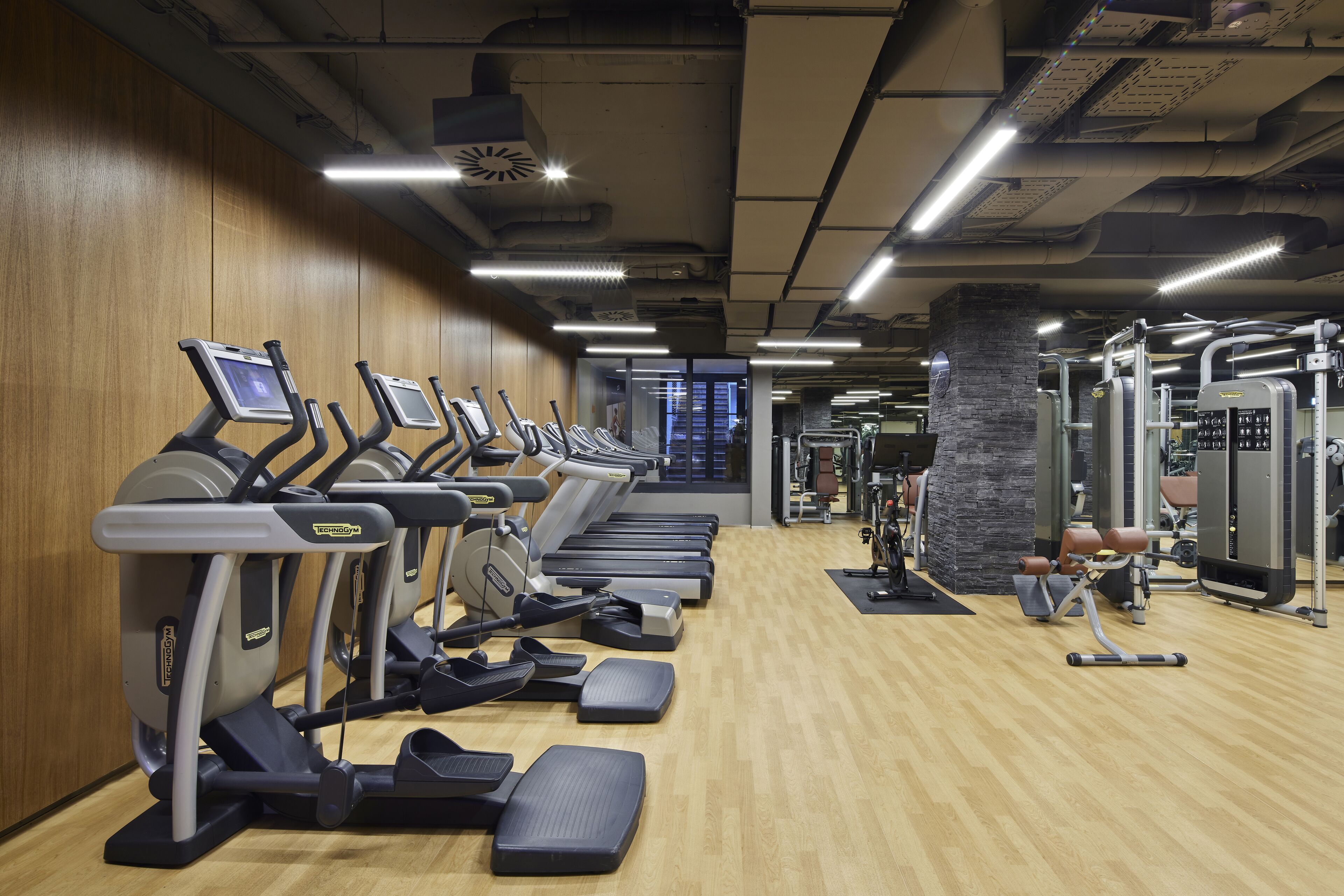 A gym with treadmills, weight machines, and a wooden floor.