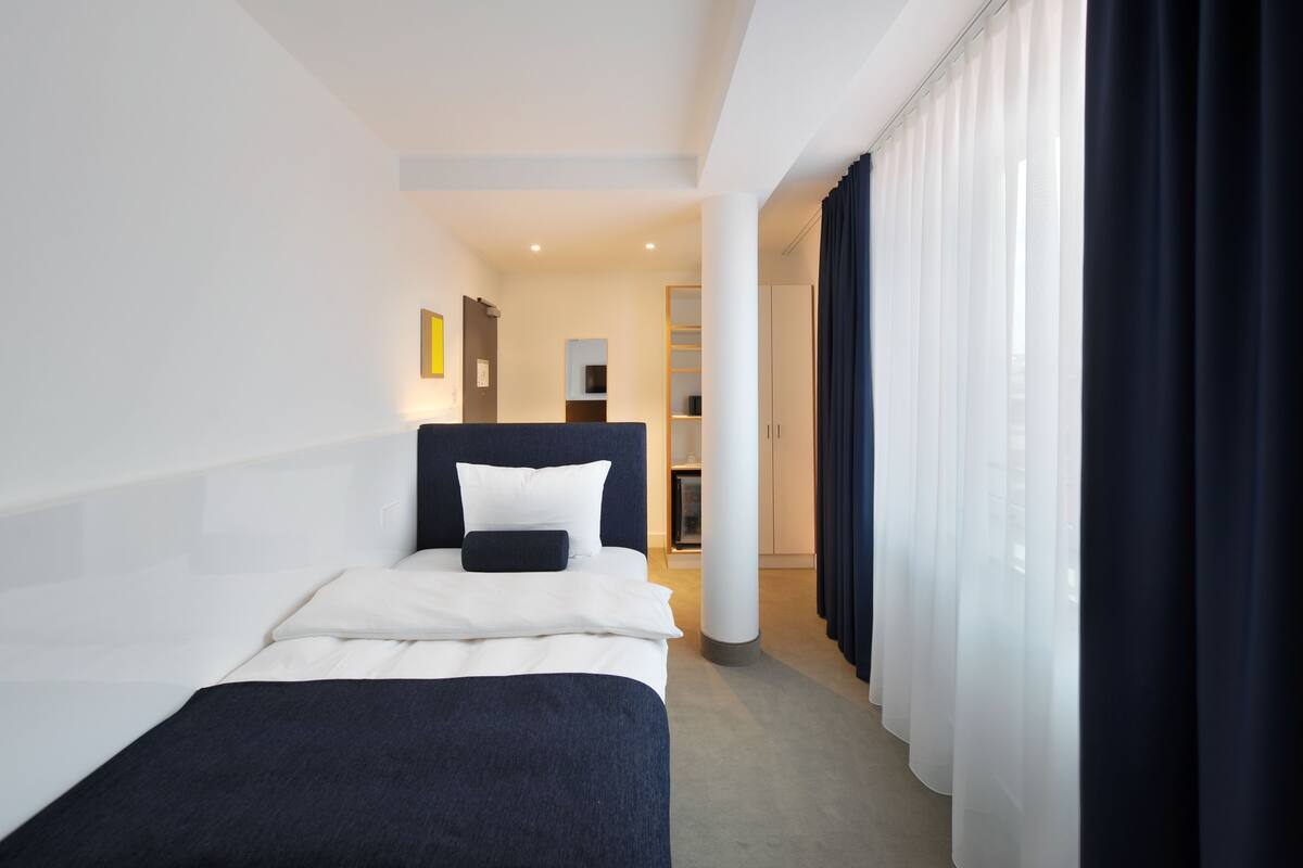 A hotel room with a bed, a nightstand, a mirror, a wardrobe, and a view of a hallway.