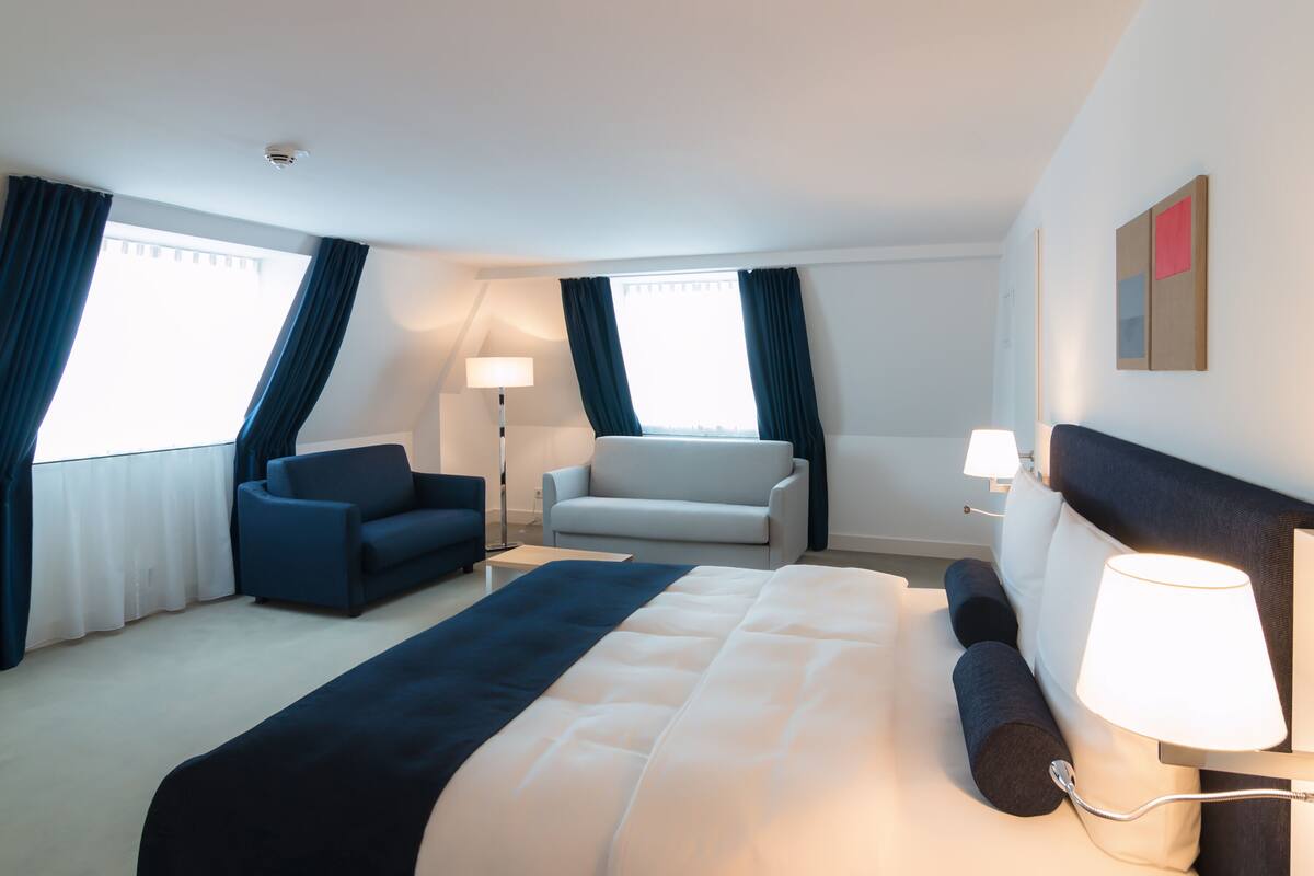 A hotel room with a large bed, a sofa, a chair, and two lamps.