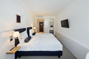 Una moderna camera d'albergo con un letto grande, un comodino, una lampada e un televisore a schermo piatto montato a parete.