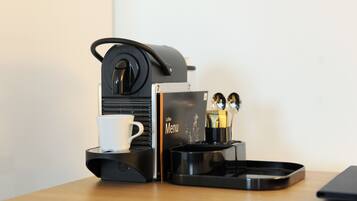 A coffee maker with a cup, a menu, and a tray with utensils on a wooden table.