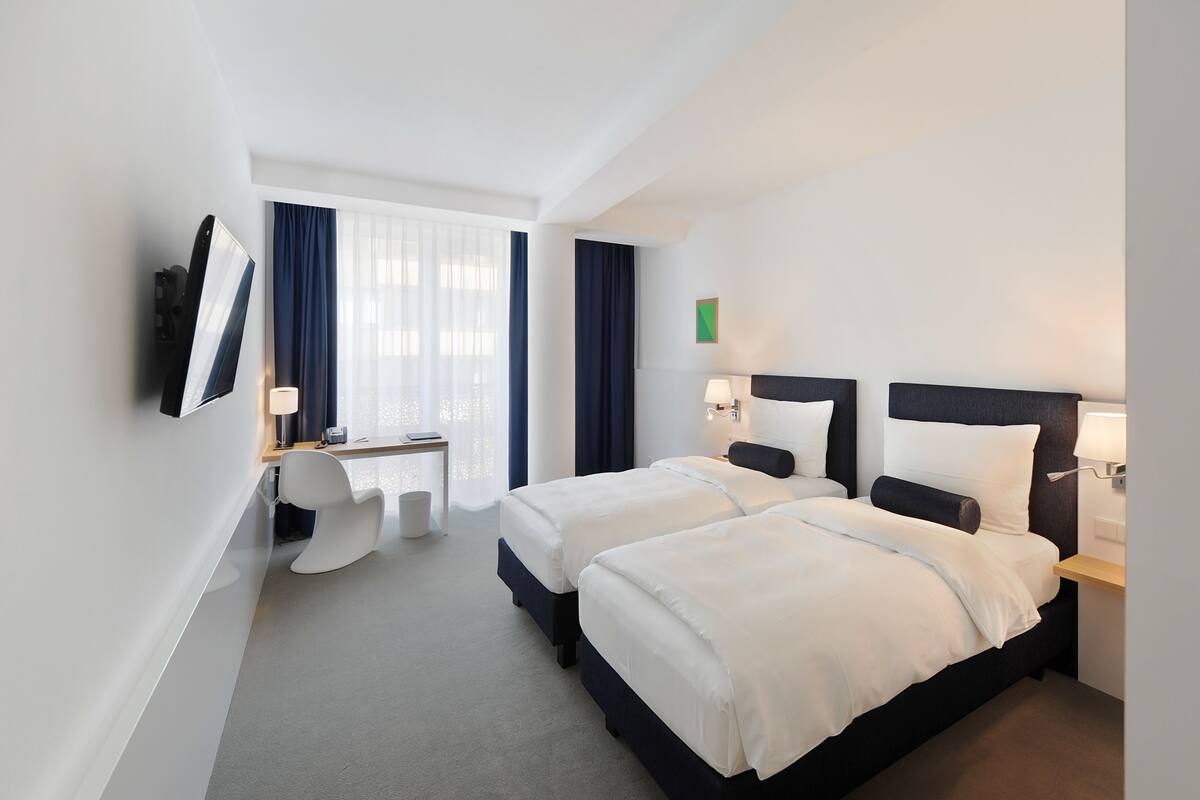 A hotel room with two beds, a desk, and a TV mounted on the wall.