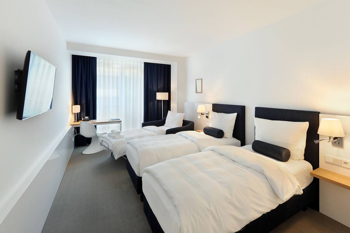 A hotel room with three beds, a TV, and a desk with a chair.