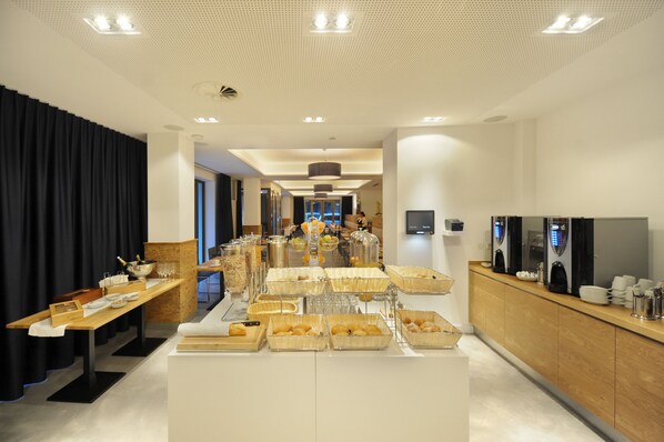 A modern hotel dining area with buffet-style food stations, a coffee bar, and a seating area with a view of the cityscape.