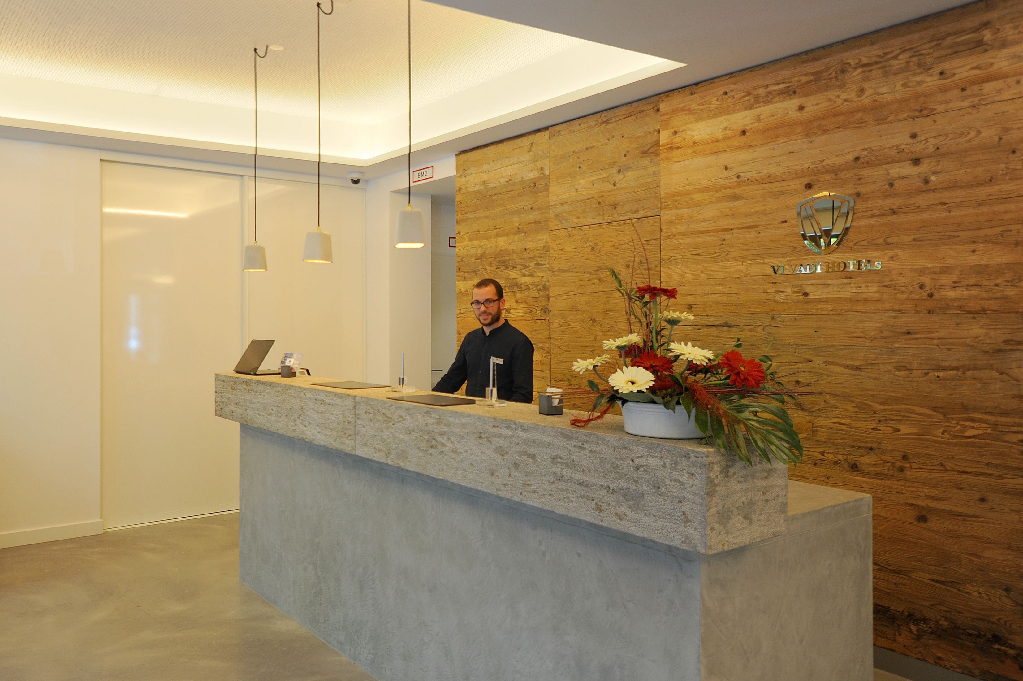 Una recepción con un panel de madera, un logotipo y un arreglo floral.