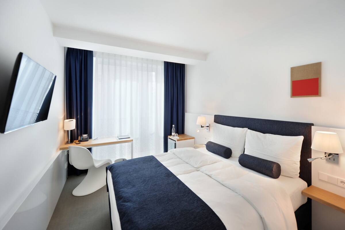 A hotel room with a bed, desk, chair, and a TV mounted on the wall.