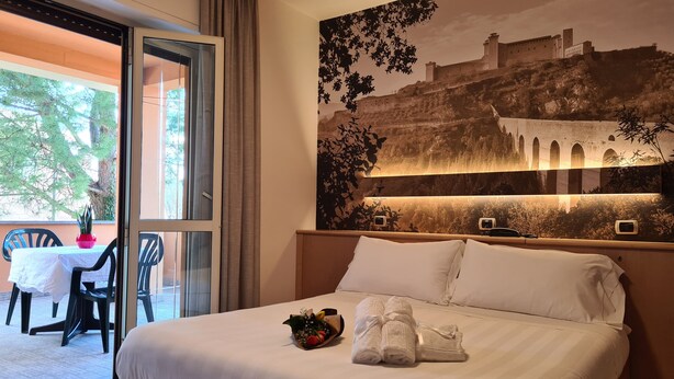 Una habitación de hotel con cama, una mesa con sillas, una planta en maceta y un mural grande con un castillo.
