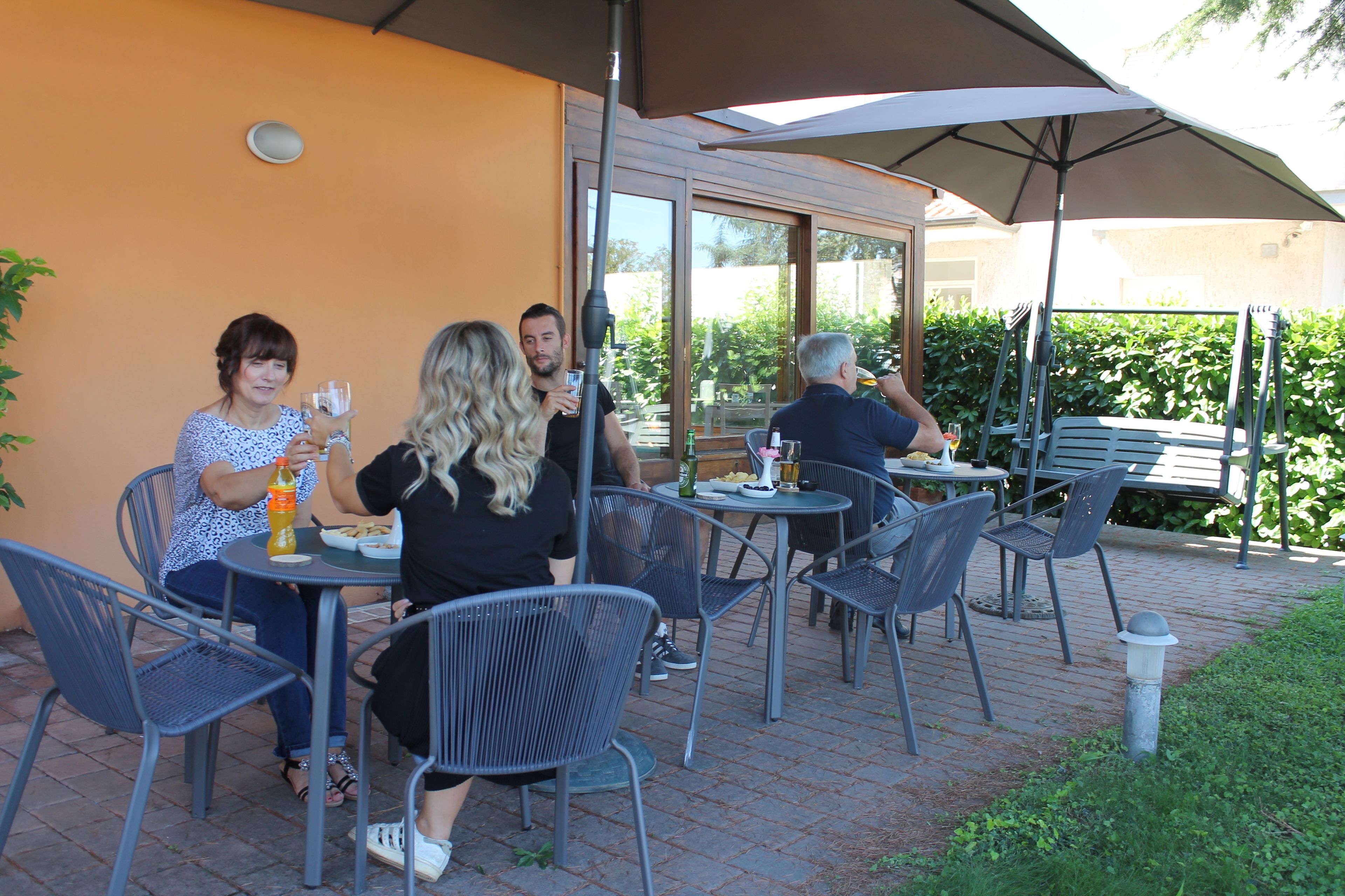 An outdoor patio with metal chairs and tables, a large umbrella, and a brick floor.