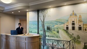 Una recepción con una computadora portátil, un florero con ramas y un mural de un paisaje con un edificio.