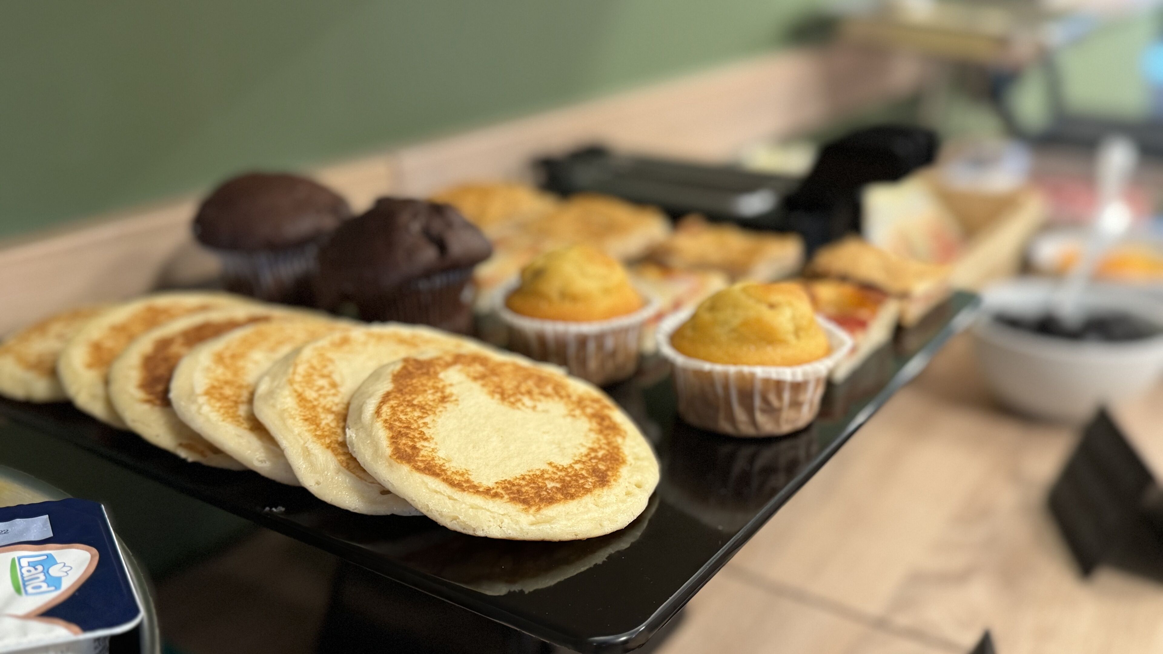 A tray of various pastries and baked goods, including pancakes and muffins, on a black tray.