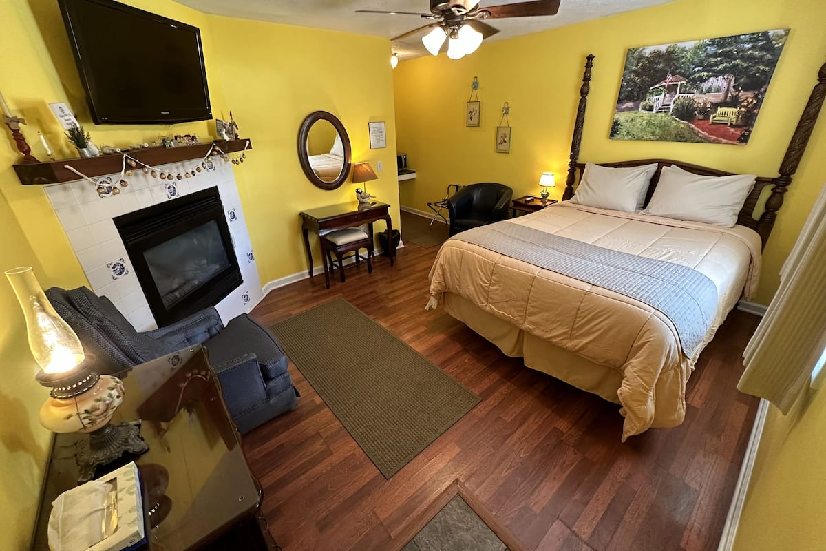 Un dormitorio con chimenea, cama, escritorio, silla y ventilador de techo.