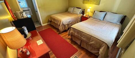 Een hotelkamer met twee bedden, een bureau met een lamp, een rode vloerkleed en een schilderij aan de muur.