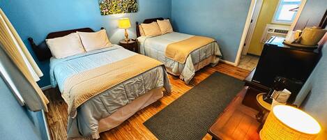 A room with two beds, a ceiling fan, a painting, a lamp, and a TV.