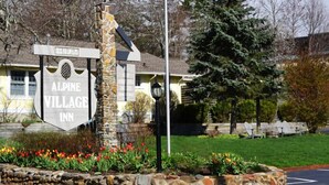 A stone sign with "Alpine Village Inn" and a gazebo in a landscaped area with a road and trees. - Alpine Village Inn (Blowing Rock)