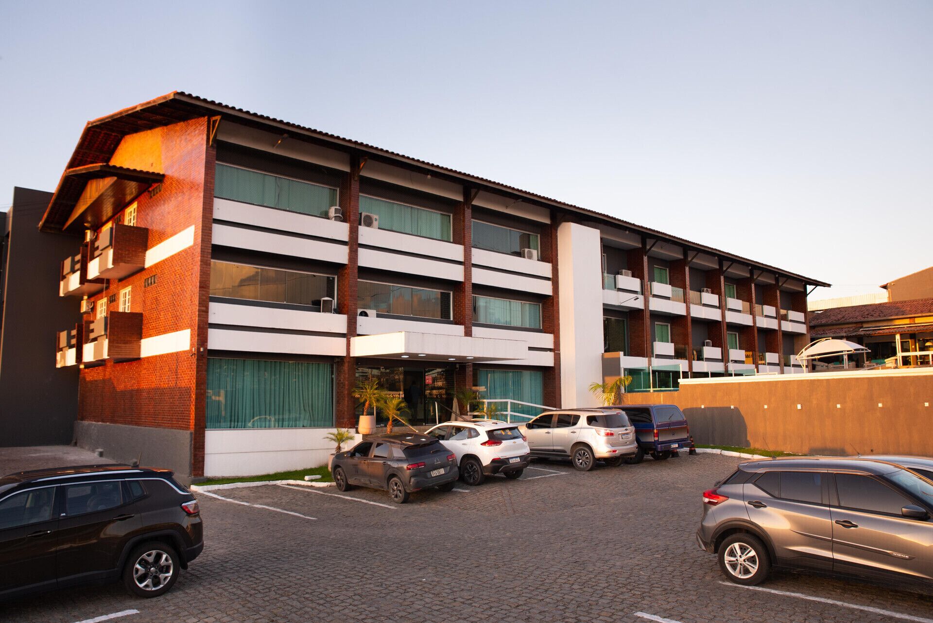 A multi-story hotel with a modern design, featuring a parking lot with several cars.